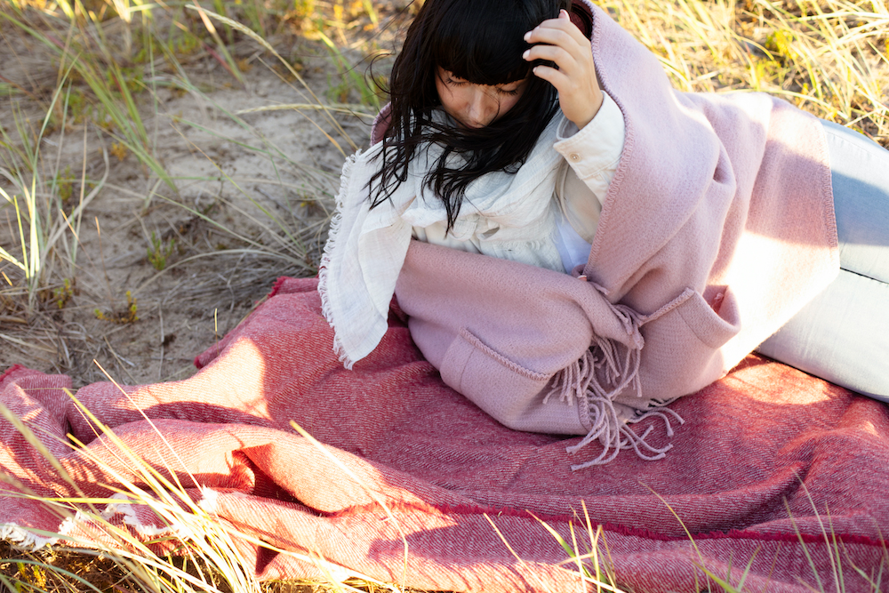 Dame med rosa ullsjal ligger på et pledd på stranden.